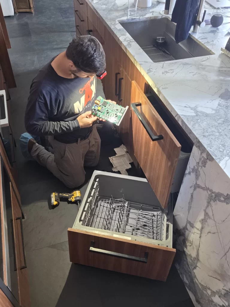 Technician holding a control board beside an open Fisher and Paykel DishDrawer