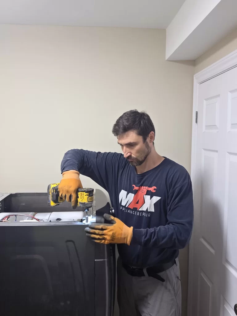 Technician removing a screw from the rear edge of the Maytag dryer top panel