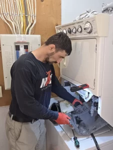 Technician holding a removed housing coated with lint beside the opened Whirlpool dryer section