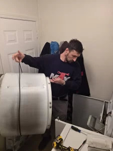 Technician holding the removed Whirlpool dryer drum with the drive belt around it