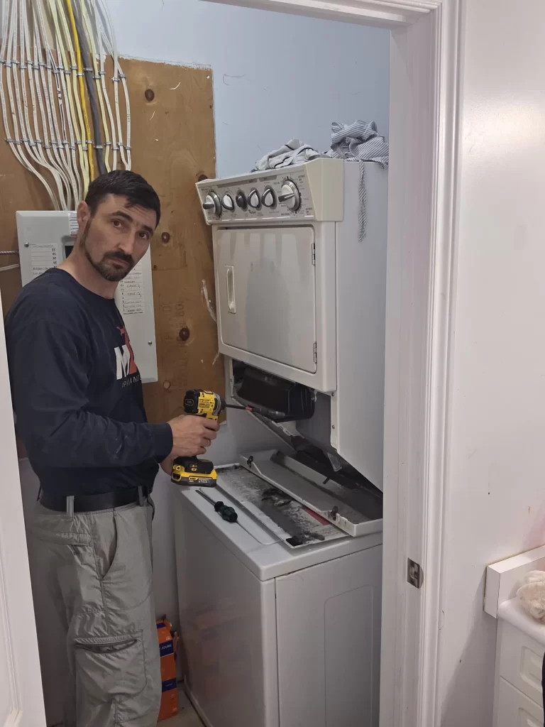 Technician beside a Whirlpool laundry center with the lower dryer access panel removed