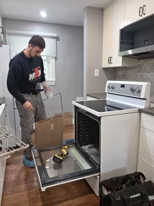 Technician holding a replacement heating element beside the open Whirlpool oven