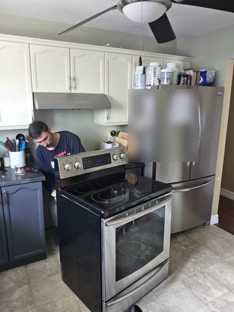 Technician working beside a Samsung electric range pulled forward for service