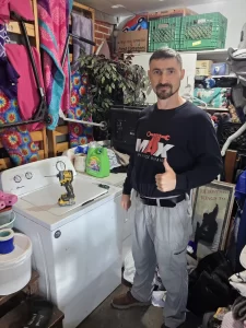 Max Appliance Repair technician beside the closed Amana top-load washer