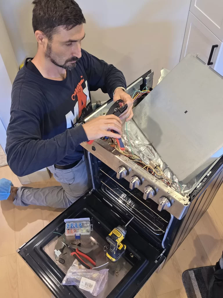 Technician working with the GE range control panel open and wiring exposed