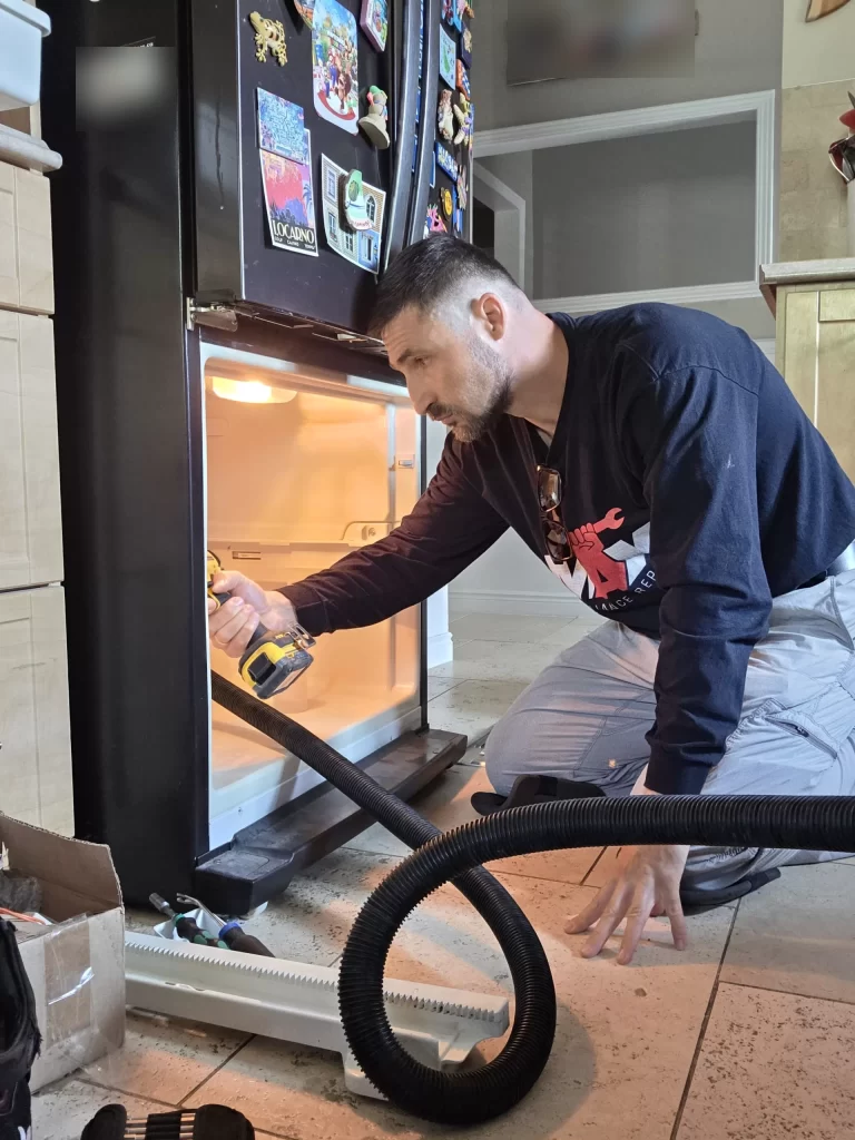 Technician using a driver inside the open Whirlpool refrigerator freezer compartment