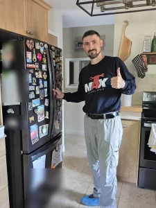 Max Appliance Repair technician beside the closed Whirlpool refrigerator after the repair